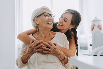 Cheerful woman hugging grandmother sitting in kitchen