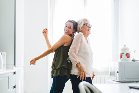 Smiling senior woman dancing with granddaughter in kitchen at home