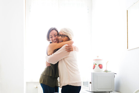 Happy grandmother hugging granddaughter in kitchen at home