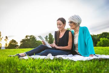 Smiling granddaughter using digital tablet while sitting by grandmother on picnic blanket