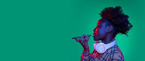 Flyer young pretty african girl, student using phone isolated on dark green studio background in...