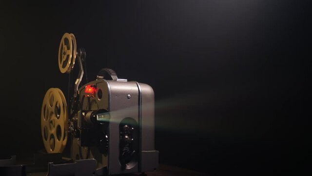 Working retro film projector, old-fashioned antique 8mm film projector projecting a color beam of light in a dark room