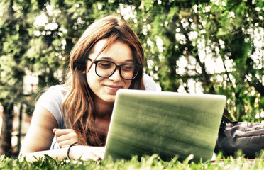 Caucasian teenager girl lying on the grass using laptop. Happiness and lightheartedness concept