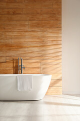 Fototapeta na wymiar White bathtub with towel near wooden wall in room