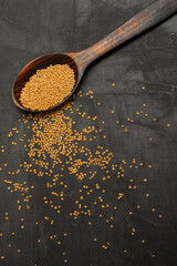Yellow Raw Organic Mustard Seeds on wooden Spoon on dark concrete background