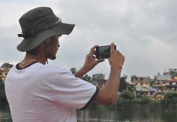 Obraz premium Back view of a male tourist taking photo of landscape with smartphone during cloudy weather 