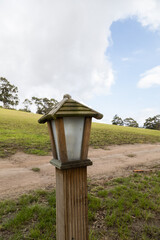 lamp with wooden house design next to a dirt road in the background mountain with grass and trees in the day, nature and object outside, decoration