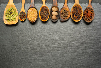 Obraz na płótnie Canvas Various herbs and spices in wooden spoons on slate board. Flat lay of spices ingredients pepper, anise star, nutmeg, allspice, clove, mustard seeds and cardamom on slate.