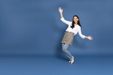 Fototapeta na wymiar Young Asian woman housewife wearing kitchen apron cooking and dancing isolated on blue background