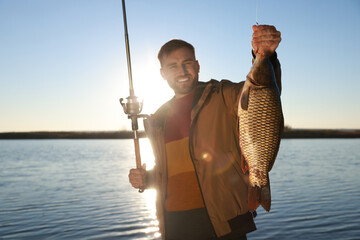 Fisherman holding rod and catch at riverside, focus on fish