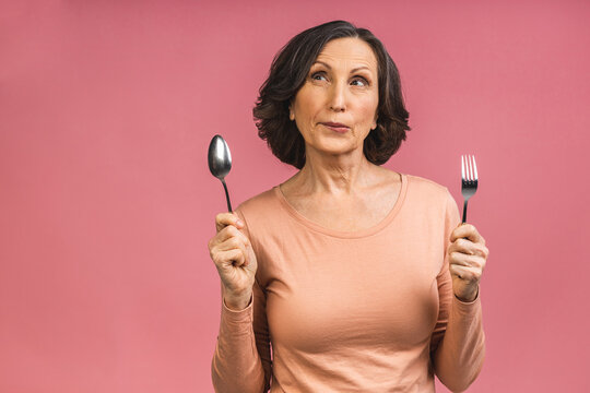 Photo Of Cheerful Aged Mature Senior Woman With Spoon And Fork Eating Delicious Healthy Meal Dieting Isolated Over Pink Color Background.