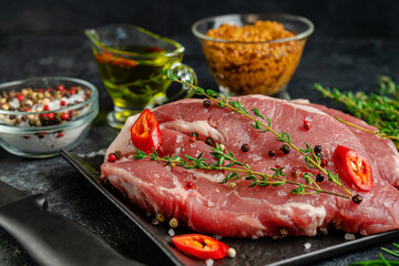 Pork steak on black slate plate with spices and herbs. Close up.