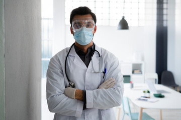 Male healthcare worker wearing protective face standing with arms crossed at hospital