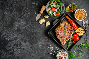 Grilled pork steak on cast iron pan with spices and vegetables on dark background. Copy space, top view