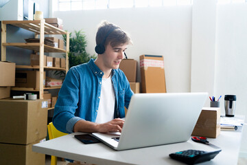 Male customer service representative wearing headphones using laptop at desk