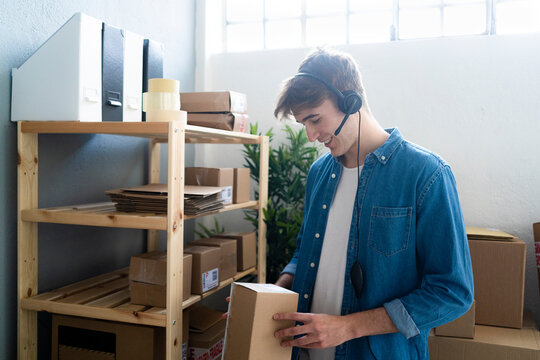 Smiling male customer service representative checking box by rack in warehouse