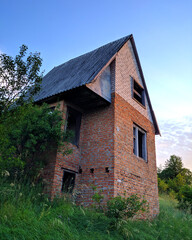 Fototapeta na wymiar Abandoned brick house with a gable slate roof overgrown with greenery