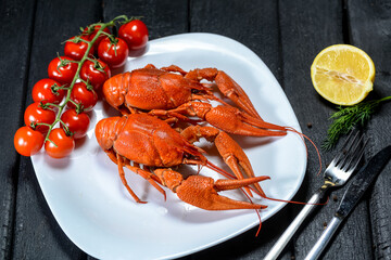 two large boiled crayfish on a white plate with a branch of cherry tomatoes on a black background
