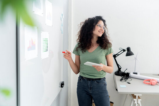 Businesswoman with digital tablet planning business strategy on whiteboard in office