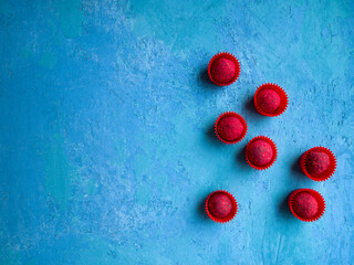 Some delicious chocolate truffles covered with raspberry sprinkle on a blue concrete background. Tasty and colorful dessert.