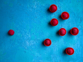 A group of crimson chocolate truffles in red wrappers opposes one raspberry truffle without a wrapper. Standoff concept.