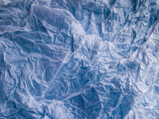 Thin white wrinkled tissue paper. A blue background shines through the crumpled paper. The texture of the material resembles tulle. Copy space. Cold mood.