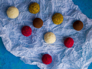 Different chocolate truffles on a crumpled paper background. Four kinds of candy: dark chocolate truffle coated cocoa, white chocolate coconut bonbon, red truffle with raspberries and pistachio candy