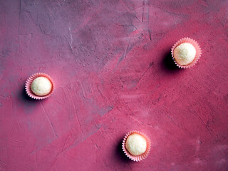 Top view on three coconut chocolate truffles on a gray and pink background. Copy space.