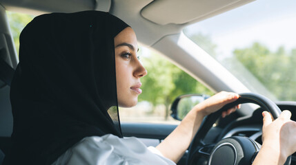 Woman in hijab looking away while driving car