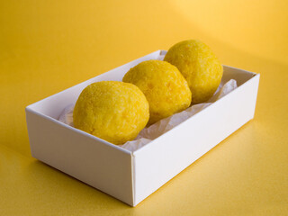 A neutral white box with three beautiful yellow citrus-flavored sweets. White chocolate truffles with orange fruit aroma on a golden background.