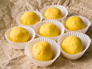 Side view of many chocolate truffles coated with freeze dried orange on crumpled brown craft paper.