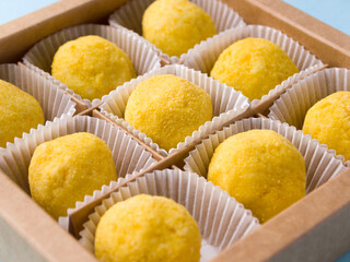 Box with white chocolate truffles coated with freeze dried (sublimated) orange powder. Nine yellow delicious sweets in white candy wrappers.