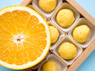 Top view of a box with bright yellow citrus flavored sweets. On top is a slice of juicy orange. Appetizing fresh dessert.