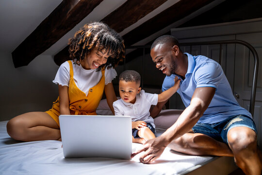 Happy family with son sitting on bed using laptop in attic at home