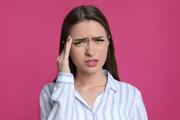 Young woman suffering from headache on pink background