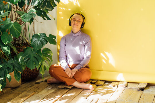 Woman listening music through headphones in front of yellow backdrop