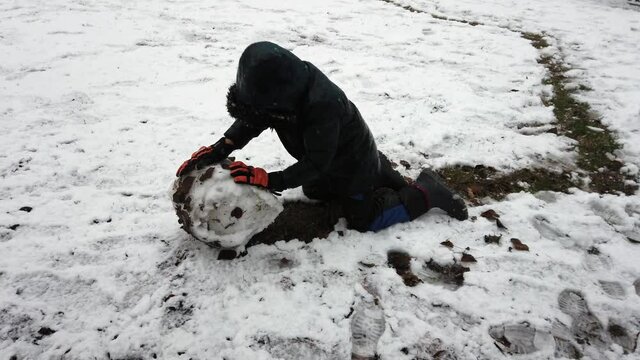 child makes a snowball to create a ship snowman - snowfall in the city in  Sempione park  of Milan on Christmas days
