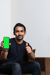 Young indian boy holding a mobile phone with a green screen on it