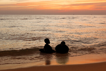 A silhouette of two boys lounging in the sea by the beach in the evening after sunset during the twilight sky.