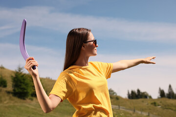 Young woman throwing boomerang outdoors on sunny day - obrazy, fototapety, plakaty