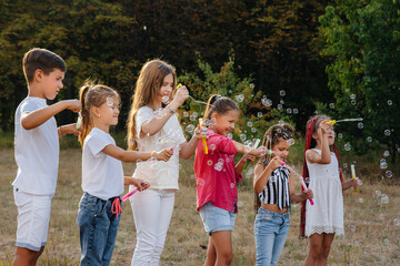 A large group of cheerful children play in the Park and inflate soap bubbles. Games in a children's camp