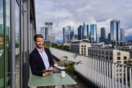 Smiling male professional sitting with digital tablet at table on rooftop