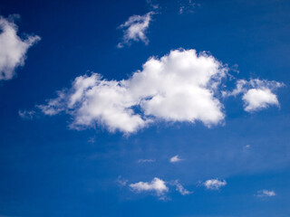 White clouds on a saturated blue sky on a bright sunny day. Natural background. View from the ground.