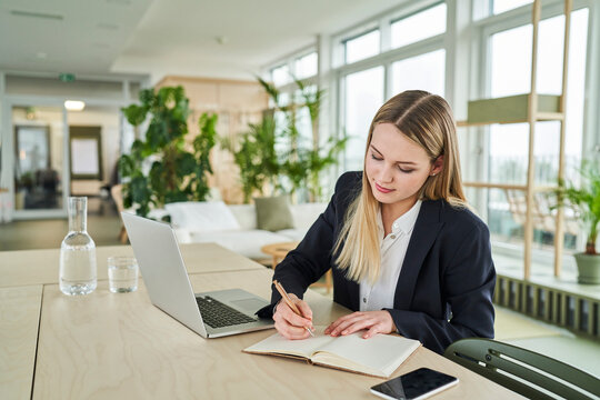 Teenage blond intern writing in diary while sitting at desk in office
