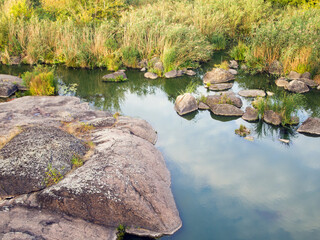 Amazing autumn nature: tall yellow dry grass and large stones near the riverbank. Plants are...