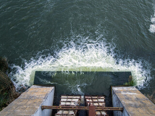 Top view from the concrete bridge of the dam on the river with a strong current. Blue water (turquoise, teal, yale, azure) with white foam. 