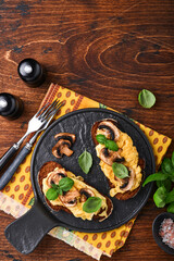 Scrambled eggs with fried mushrooms and basil on bread on black table background. Homemade breakfast or brunch meal - scrambled eggs and mushrooms sandwiches. Top view with copy space