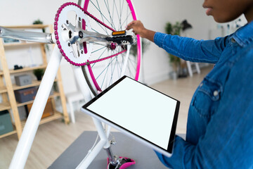 Young woman with digital tablet repairing bicycle at home
