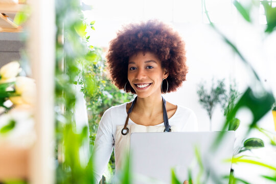 Female shop owner with laptop smiling at plant store