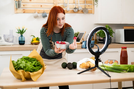 Woman showing strawberry while live streaming through mobile phone in kitchen